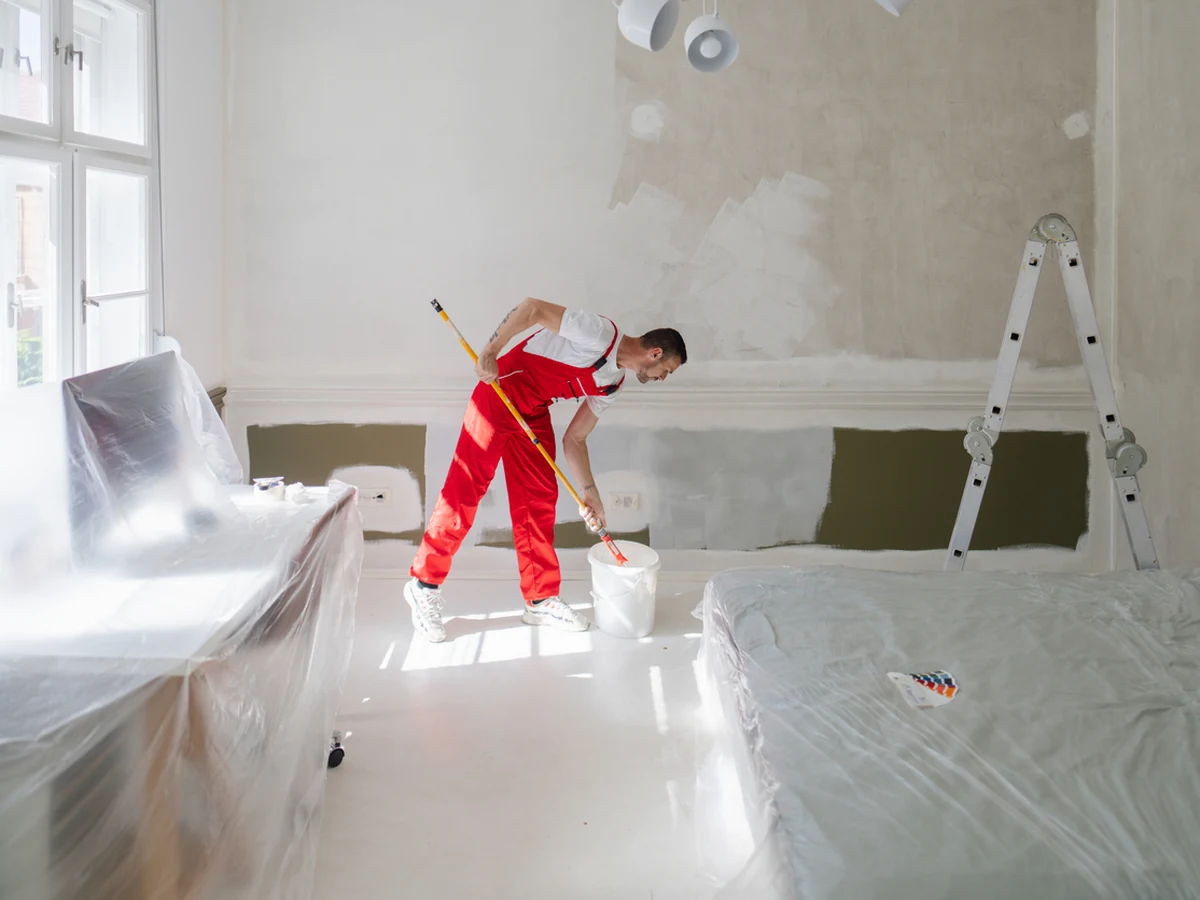 Bath Decorators painter in red overalls applying heat-resistant coating to radiator